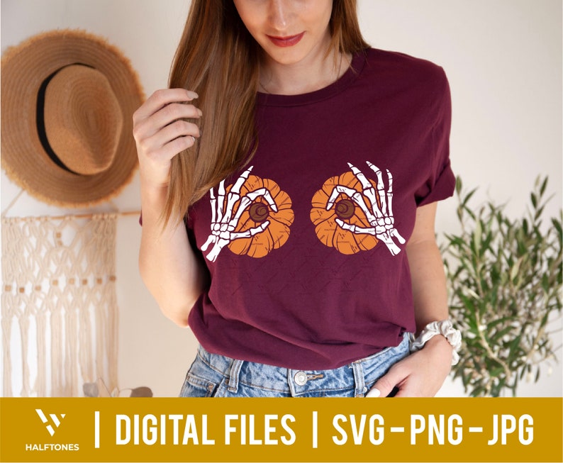 May include: A maroon t-shirt with a graphic of two skeleton hands holding pumpkins. The pumpkins are orange with a brown stem and a black seed inside.