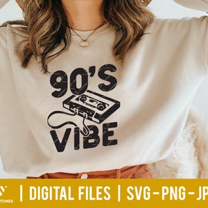 Op de afbeelding: Een beige sweatshirt met een zwart grafisch ontwerp dat "90's Vibe" zegt met een vintage cassetteband-afbeelding.