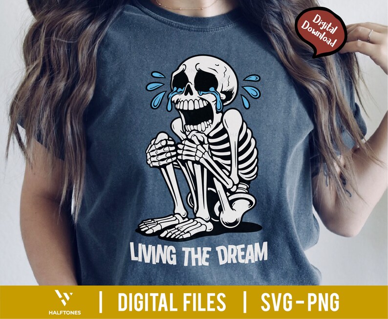 May include: A dark blue t-shirt featuring a crying skeleton illustration. The skeleton is white with black outlines, and blue tears are streaming from its eyes. The text "LIVING THE DREAM" is printed in white below the skeleton.