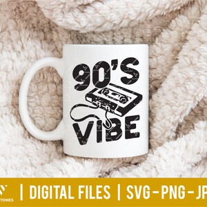 Pu&ograve; includere: Tazza in ceramica bianca con un design grafico nero che dice "90's Vibe" con un grafico di cassetta retr&ograve;.