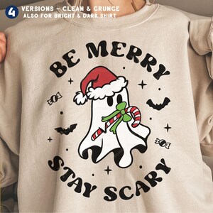 May include: Beige sweatshirt with a graphic of a ghost wearing a Santa hat and holding a candy cane. The text "BE MERRY STAY SCARY" is in a circular design around the ghost. Includes bats, candy, and stars.
