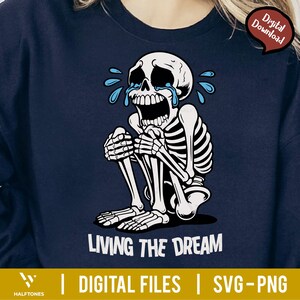 May include: Navy blue sweatshirt featuring a crying skeleton illustration. The skeleton is seated, with tears and the text "LIVING THE DREAM" in white. The design includes "DIGITAL FILES | SVG-PNG" at the bottom, with a "Digital Download" tag.
