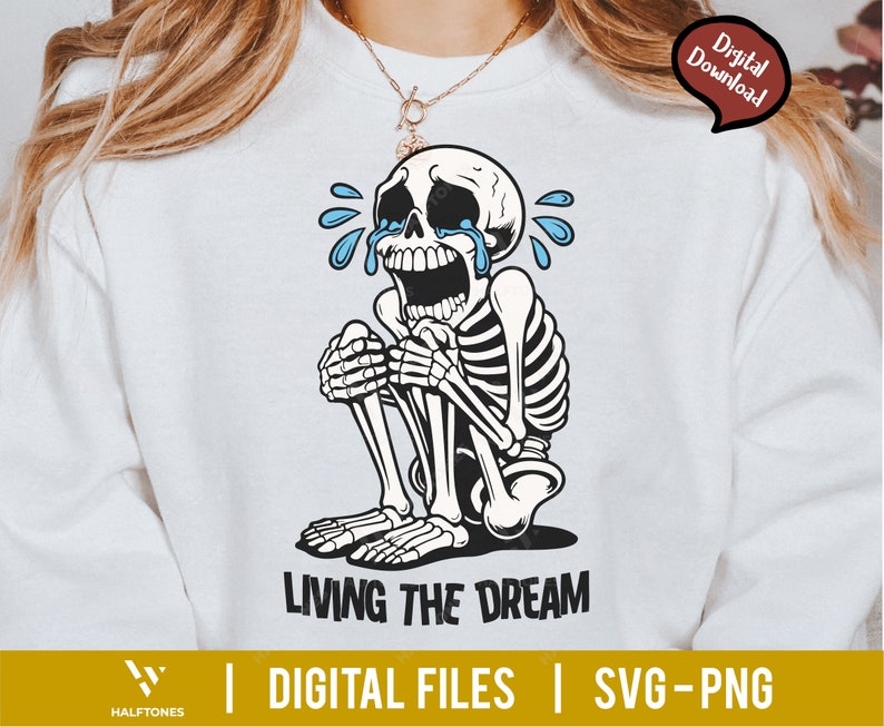 May include: White sweatshirt featuring a crying skeleton illustration with blue tears. The skeleton is sitting with its knees up, and the text "LIVING THE DREAM" is below. The image also includes the text "DIGITAL FILES | SVG-PNG".