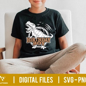 May include: A black t-shirt with a white dinosaur graphic and the text "Birthday Boy" in brown letters. The dinosaur is surrounded by a brown circle with a white outline.