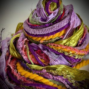 Puede incluir: Un conjunto de cintas e hilos decorativos variados en una paleta de colores vibrantes que incluye morado, verde lima, naranja y rosa. La colección presenta diversas texturas, como satén liso, felpilla suave, cordón trenzado y bordes deshilachados.