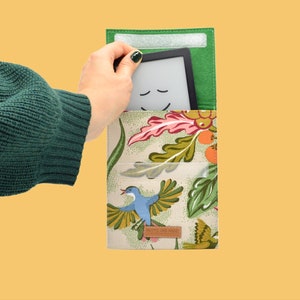 Könnte beinhalten: Eine grüne Filz-E-Reader-Hülle mit einem Blumenmuster mit Vögeln und Blättern. Die Hülle hat eine Klappe, die mit Klettverschluss geschlossen wird, und eine Tasche für einen E-Reader.