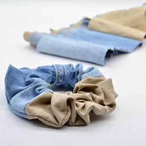 Könnte beinhalten: Ein blaues und beiges Haargummi aus recyceltem Denim und Stoff. Das Haargummi ist ein beliebtes Haaraccessoire.