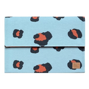Può includere: Una custodia per laptop di colore azzurro chiaro con un design a stampa leopardata. La custodia ha una toppa in pelle marrone con il testo "Nutti und Madi" su di essa.