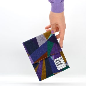Könnte beinhalten: Eine bunte geometrische Stofftasche mit einem weißen Etikett, auf dem "MUTTI UND MADI" und "HANDGEMACHT" steht.