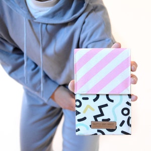 Könnte beinhalten: Eine kleine, rechteckige Tasche mit einem rosa-weiß gestreiften Oberteil und einem weißen Unterteil mit einem schwarz-weißen geometrischen Muster. Die Tasche hat ein braunes Leder-Etikett mit dem Text "ROTTE UNO MAD" darauf.