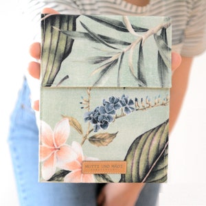 Könnte beinhalten: Eine grüne Stofftasche mit einem Blumendruck mit rosa, blauen und grünen Blumen. Die Tasche hat ein braunes Leder-Etikett mit der Aufschrift "MUTTI UNO MADE HANDMADE".