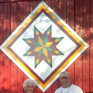May include: A red barn with a large, white diamond-shaped quilt block painted on the side. The quilt block features a colourful star with yellow, green, and brown points.