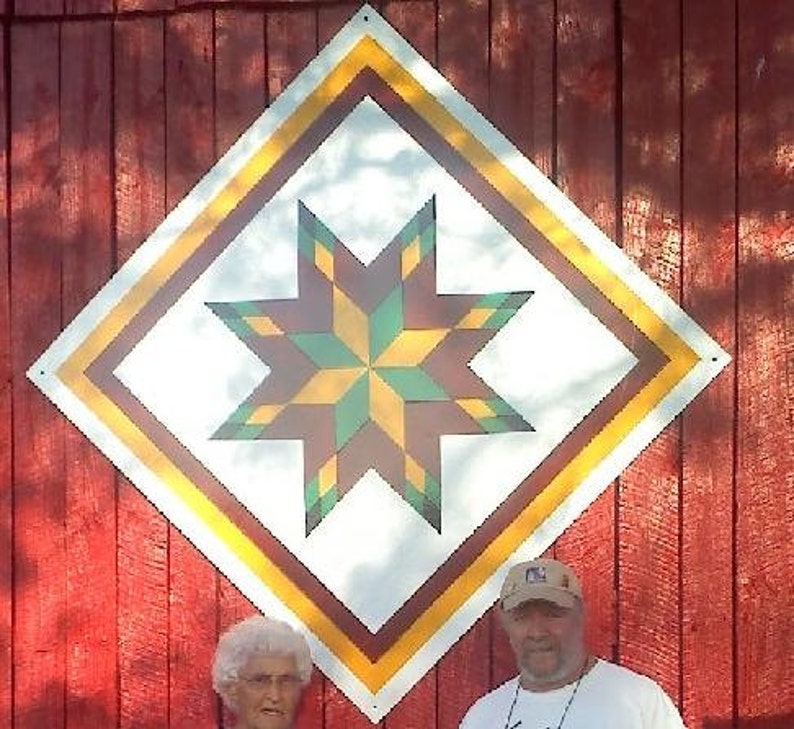 May include: A red barn with a large, white diamond-shaped quilt block painted on the side. The quilt block features a colourful star with yellow, green, and brown points.