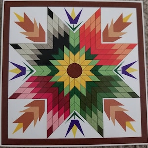 May include: A colourful quilt block featuring a star design. The star is composed of various shades of red, green, yellow, and brown. The centre of the star has a sunflower design with a brown centre and yellow petals. The corners of the block have a design of wheat stalks in shades of brown.