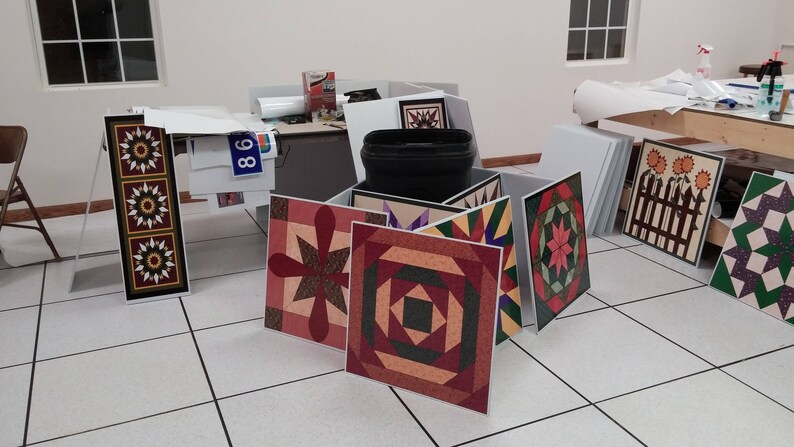 May include: A collection of colourful quilt blocks with geometric patterns, including a red and green block with a star, a red and black block with a square, and a purple and green block with a diamond. The blocks are arranged on a white tiled floor.