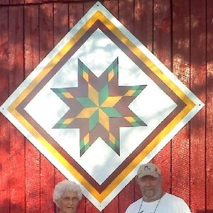 May include: A red barn with a large, white diamond-shaped quilt block painted on the side. The quilt block features a colorful star with yellow, green, and brown points.