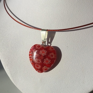 May include: A red heart-shaped pendant necklace with a white floral pattern. The necklace is made of a thin, red cord.