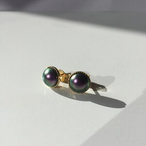 Può includere: Un paio di orecchini a bottone dorati con pietre rotonde iridescenti di colore verde e viola.