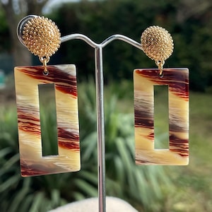 Op de afbeelding: Een paar gouden en bruine rechthoekige oorbellen met een getextureerde gouden bovenkant en een bruin en wit gestreept patroon.