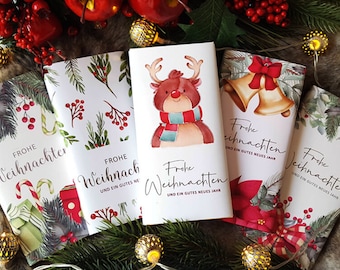 Pode incluir: Várias embalagens de barras de chocolate com tema natalino com designs festivos. Uma apresenta uma rena com um cachecol, outras têm sinos, azevinho e outros motivos festivos. O texto "Frohe Weihnachten" é visível em cada embalagem.