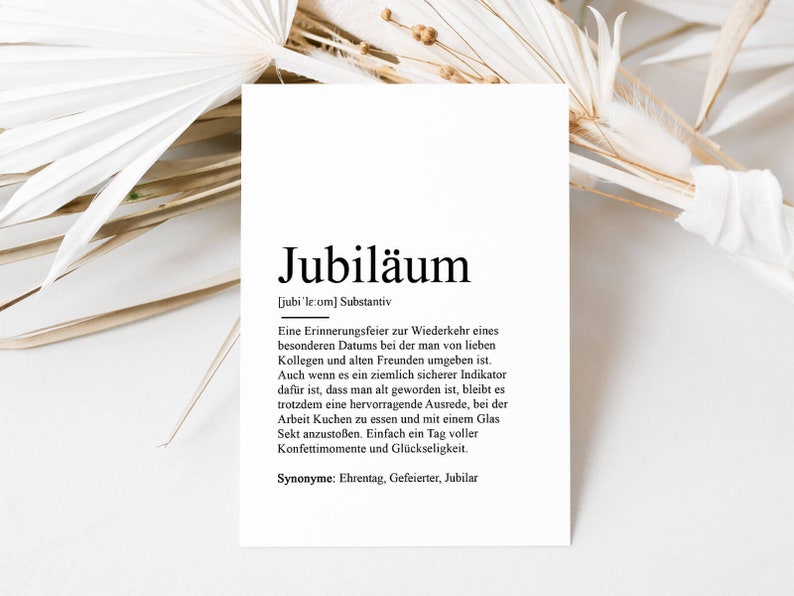May include: A black and white printable art print with the German word "Jubil&auml;um" defined as a celebration of a special date with friends and colleagues. The print includes the definition, synonyms, and pronunciation of the word.