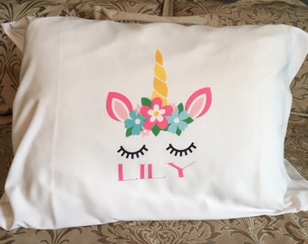 May include: White pillowcase with a unicorn design featuring a pink flower crown, closed eyes, and a gold horn. The name "LILY" is printed in pink below the unicorn.