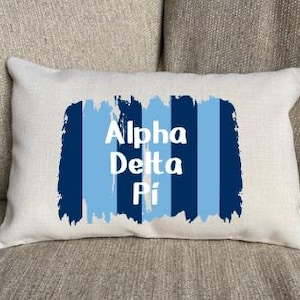 Peut inclure: Un coussin blanc avec des rayures bleues et blanches et le texte "Alpha Delta Pi" en blanc.