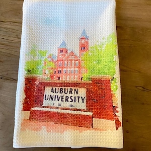 May include: White kitchen towel with a watercolor illustration of a brick building with a sign that reads "Auburn University".