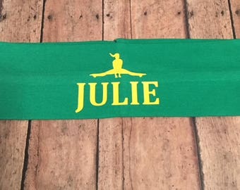 May include: Green headband with a yellow silhouette of a person doing a split and the name "JULIE" embroidered in yellow.