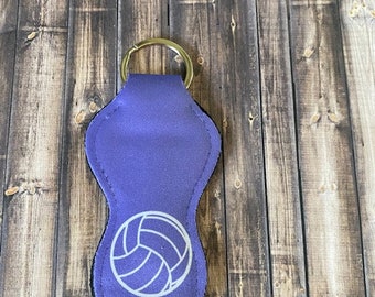 Op de afbeelding: Paarse sleutelhanger met een witte volleybal en het woord "RAIDERS" erop gedrukt.