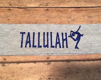 以下が含まれることがあります： グレーのヘアバンド。名前「TALLULAH」は濃い青色のグリッター文字で、フィギュアスケーターのシルエットが描かれています。柔らかい生地で作られており、スポーツや普段使いに適しています。