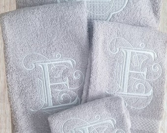 May include: Set of four gray towels with white embroidered letter E in a decorative font. The towels are arranged in a stack, with the largest towel on the bottom and the smallest towel on top.