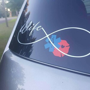 May include: A silver infinity symbol with the word "life" written inside. The symbol is centered on a car window and has a red and blue medical symbol and a red firefighter symbol inside the loop.