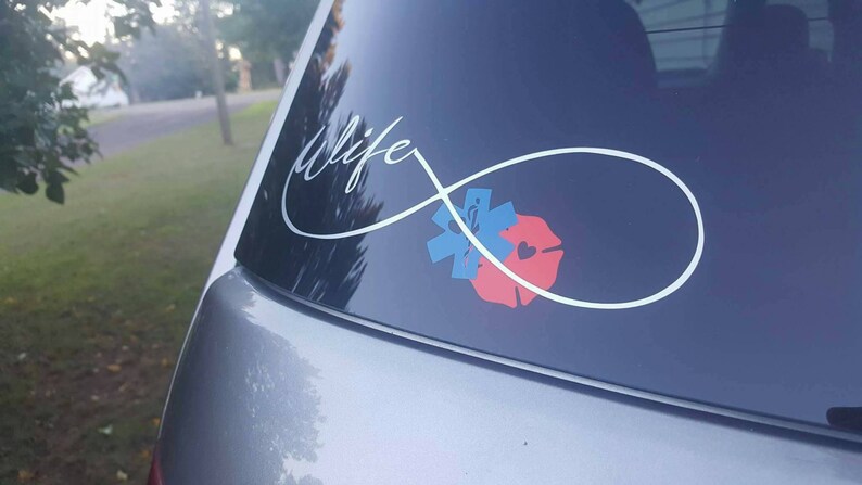 May include: A silver infinity symbol with the word "life" written inside. The symbol is centered on a car window and has a red and blue medical symbol and a red firefighter symbol inside the loop.