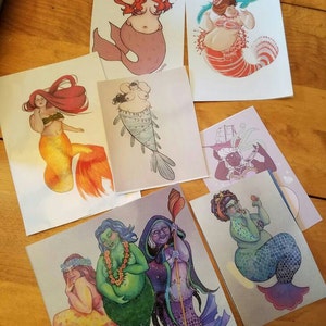 May include: Set of six illustrated cards featuring mermaids with different body types, hair colors, and tail designs. The cards are printed on white cardstock and have a matte finish.