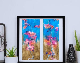 Op de afbeelding: Een paar abstracte schilderijen in zwarte lijsten. De schilderijen zijn een mix van blauwe, roze en gouden kleuren. De schilderijen worden gescheiden door een dunne zwarte lijn.