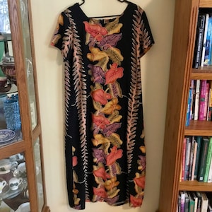 May include: A black, knee-length dress with a square neckline and short sleeves. The dress features a vibrant floral pattern in shades of red, orange, yellow, and purple. The floral design is set against a dark background, creating a striking contrast. The dress is hanging on a hanger.