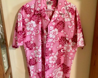 Op de afbeelding: Roze overhemd met korte mouwen en knopen met een witte hibiscus bloemenprint. Het overhemd heeft een roze achtergrond met rode bladeren en witte bloemen.