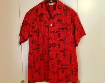 Op de afbeelding: Een rood, kort mouwig overhemd met knopen en een zwart-wit patroon. Het overhemd heeft een kraag en een zak aan de linkerkant. De tekst "Made in Korea" is zichtbaar op het label.