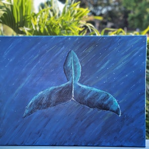Puede incluir: Una pintura sobre lienzo representa la cola de una ballena en tonos azules y turquesas sobre un fondo azul oscuro con puntos blancos en forma de estrellas. La obra de arte est&aacute; situada sobre un fondo de follaje verde.