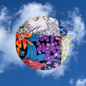 May include: A round, colorful patchwork fabric ornament with a variety of floral patterns in shades of blue, green, orange, purple, and white. The fabric is sewn together in a circular shape, creating a unique and eye-catching design.