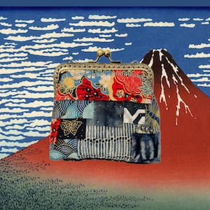 Può includere: Un piccolo porta monete in tessuto patchwork con una chiusura in ottone. Il porta monete è decorato con una varietà di tessuti colorati, tra cui rosso, blu e oro. Il porta monete è posizionato davanti a uno scenario di montagna in stile giapponese.