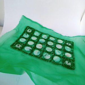 May include: A green fabric with a beaded design featuring a grid of white oval-shaped stones. The stones are surrounded by green beads.