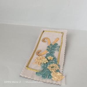May include: A beige fabric patch with a gold embroidered border. The patch features a gold and green floral design with sequins and a letter "Y" in the center.