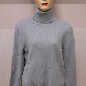 May include: A light blue ribbed turtleneck sweater. The sweater has long sleeves and a ribbed collar.