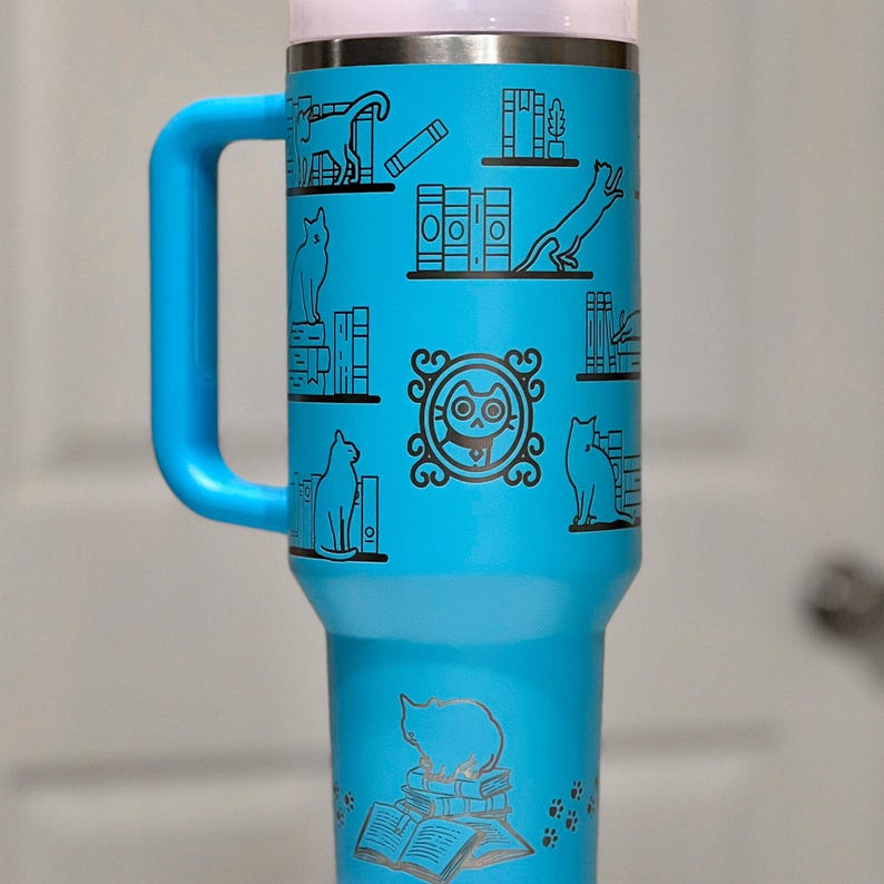 a blue travel mug with cats and books on it