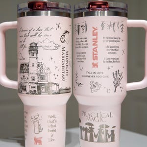 May include: Two pink Stanley travel mugs with silver accents and handles. One mug features a lighthouse illustration and the words "Midnight Margaritas!". The other mug has botanical illustrations and the text "Practical Magic".
