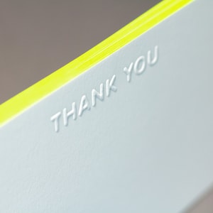 Peut inclure: Une pile de cartes gris clair avec des bords jaune vif. Le texte en relief "THANK YOU" est visible sur le devant des cartes. Ces cartes sont probablement utilisées pour exprimer sa gratitude.