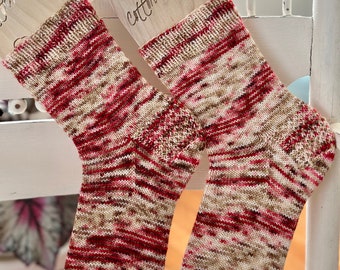 May include: A pair of hand-knitted socks in a red, brown, and white color pattern. The socks are displayed on wooden sock blockers with the text "cotton + yarn" on one of the blockers.