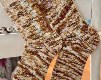 May include: A pair of brown, white, and pink patterned socks with a knitted texture. The socks are displayed on a wooden tag with the text "cotton bloom" written on it.